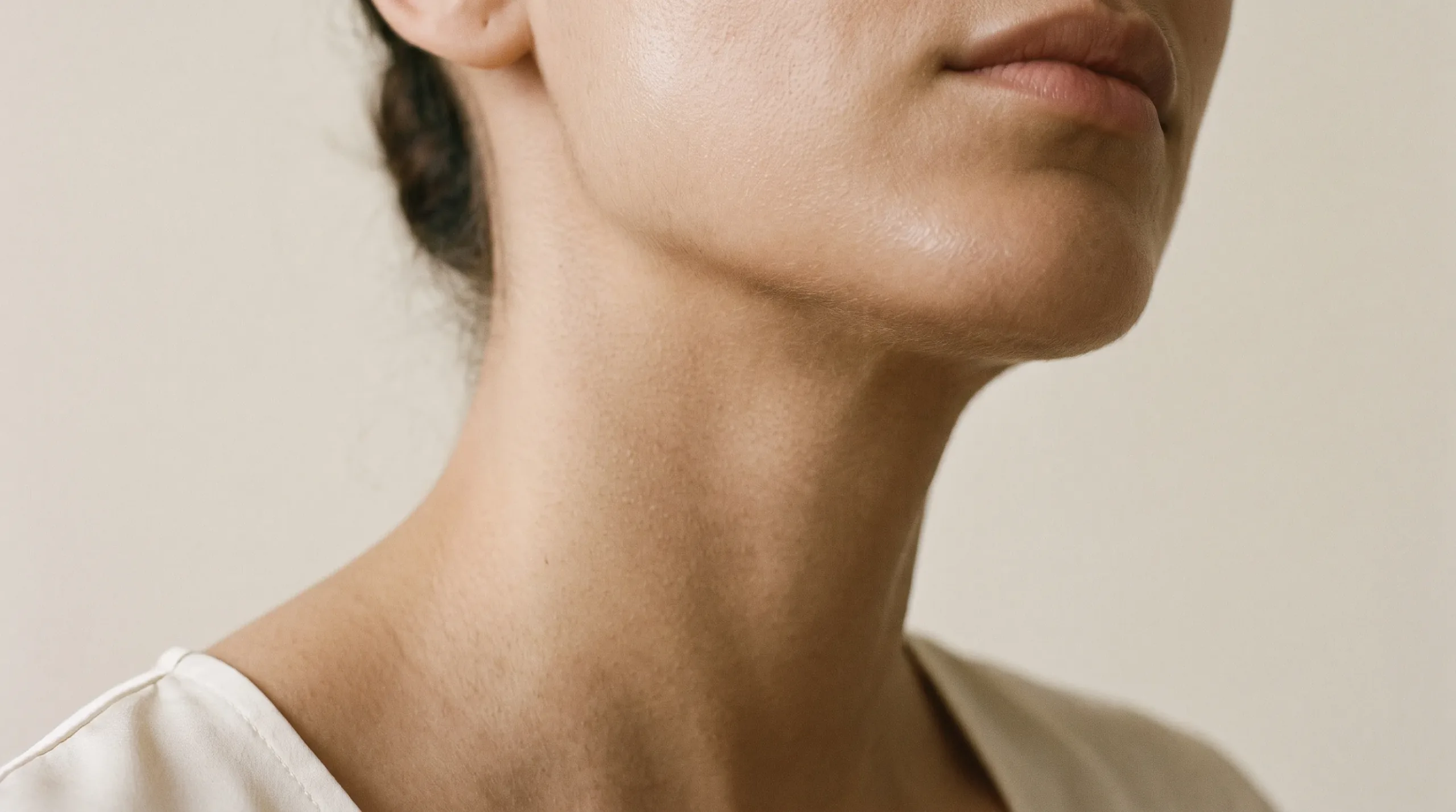 Close detail of a woman's jaw and neck in soft window light, pores and fine texture visible