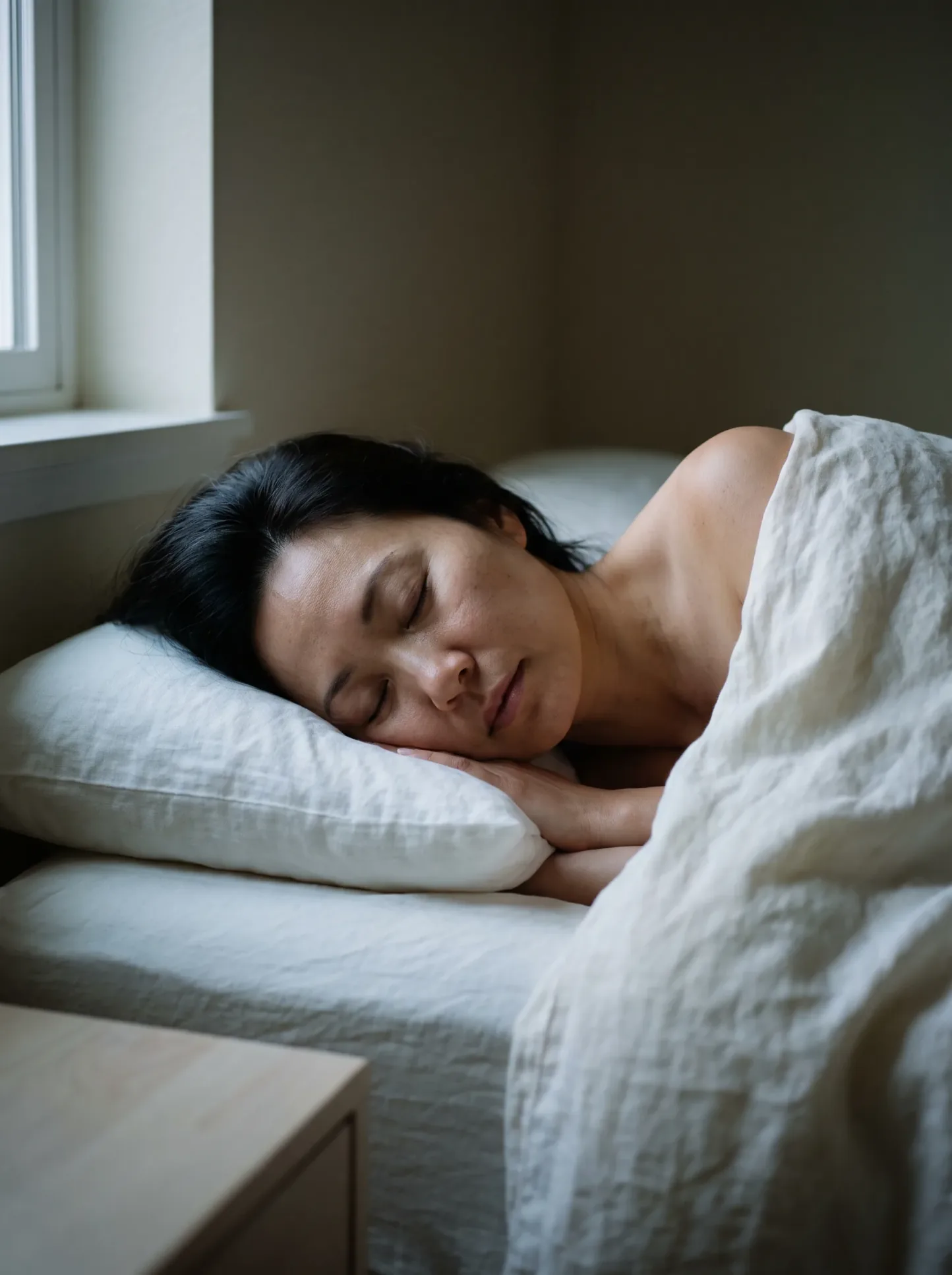 A woman asleep, covered in ivory linen, during the hours of overnight repair